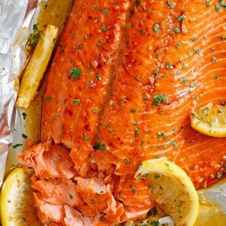 Salmon fillet in foil, with honey garlic sauce and topped with lemon wedges.