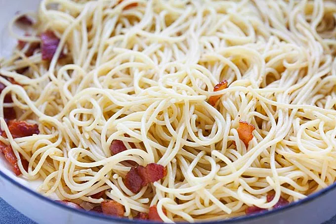 Mixing spaghetti with crispy bacon for spaghetti carbonara.