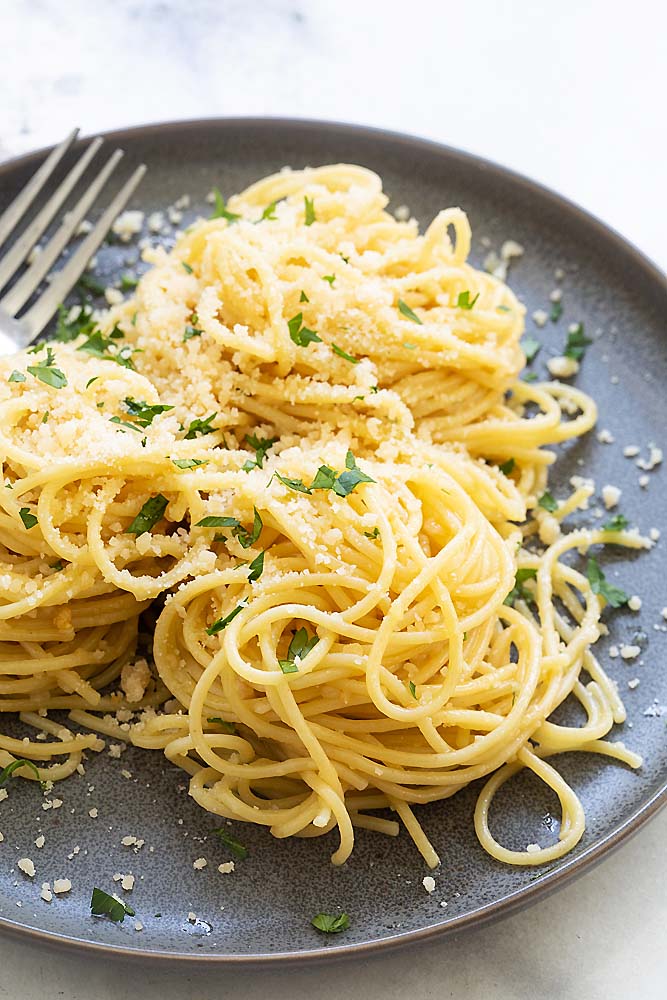 overhead image of cooked spaghetti sprinkled with Parmesan cheese and fresh herbs