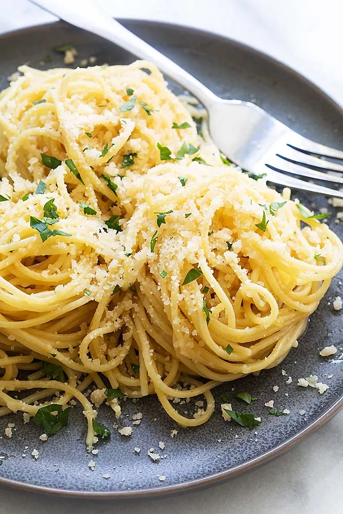 close up image of plated spaghetti tossed with olive oil and sprinkled with Parmesan cheese